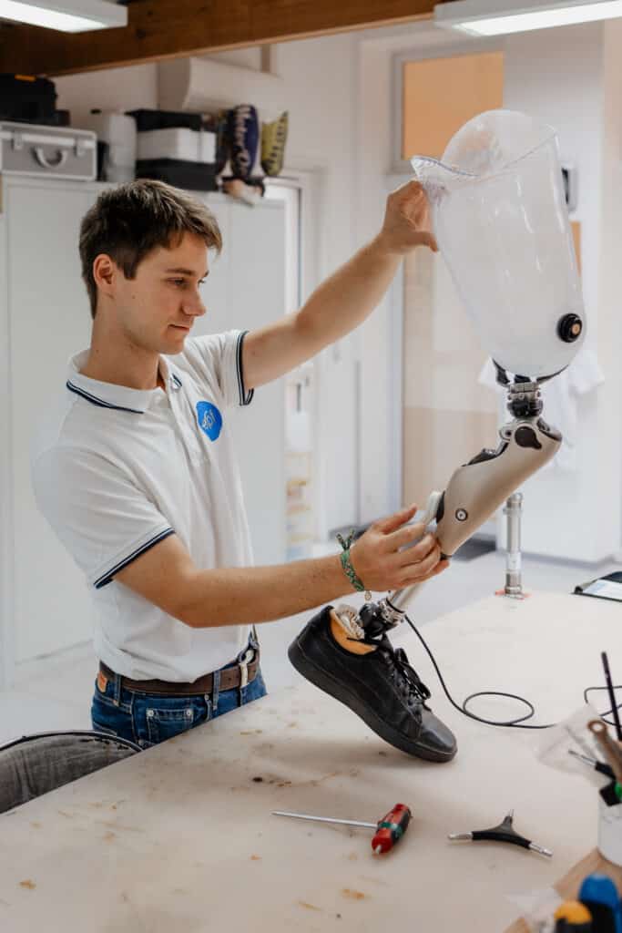 Prothésiste concentré ajustant une prothèse de jambe high-tech. Il tient un pichet clair au-dessus de l'emboîture lors du réglage en atelier.