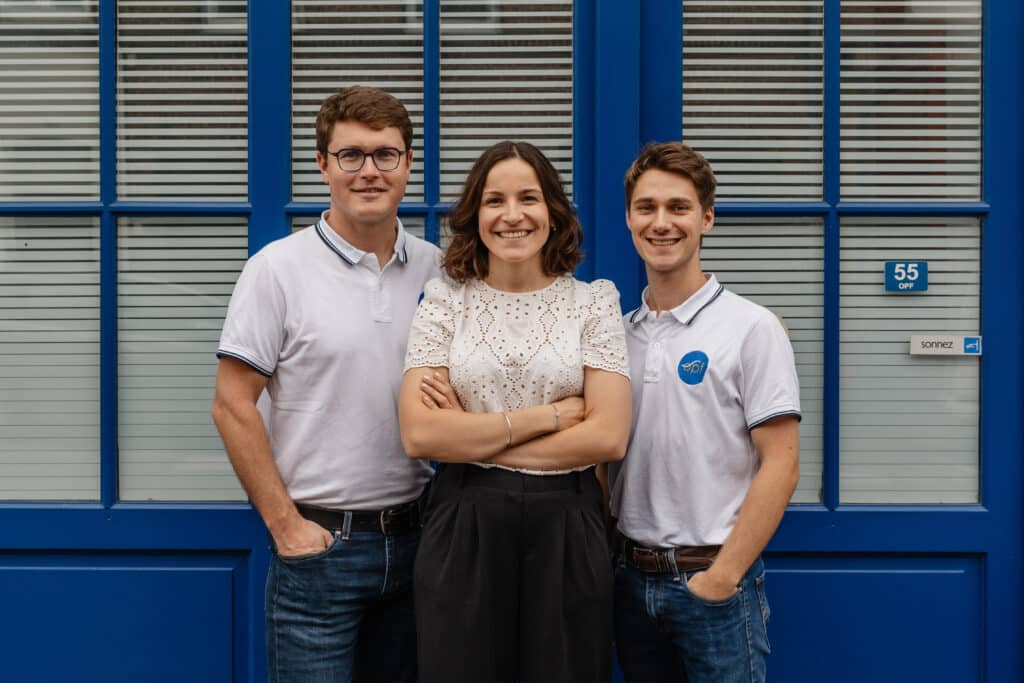 Trois professionnels OPF souriants (deux hommes, une femme) en polos blancs devant la porte bleue. Plaque 55 OPF visible; sonnez.